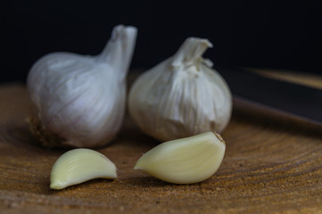 Two Garlic Cloves and Garlic Bulbs on a wooden plate and dark background. Concept for healthy eating.