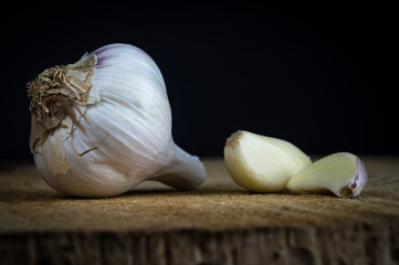 Two Garlic Cloves and Garlic Bulb on a wooden plate and dark background. Concept for healthy eating.