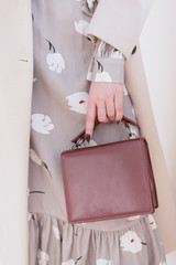 burgundy bag in hand. Vertical photo of a girl in a gray dress and a beige coat. without face