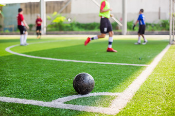 soccer ball on green artificial turf at corner of football field with blurry players background