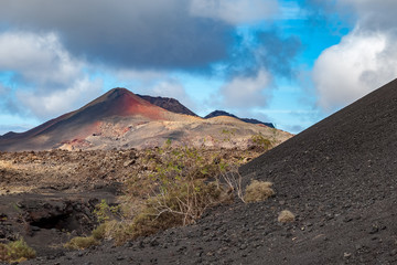 A volcanic landscape with a mountain peak with orange sand. There is blue sky with clouds in the background. Taken in Lanzarote, Canary Islands.