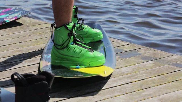 On the edge of pier man's legs, wearing green boots and shorts, are standing on water wakeboard getting ready to take a jump into the water for wakeboarding