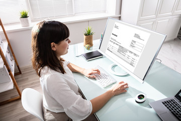 Businesswoman Calculating Invoice On Computer