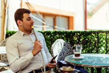 Urban man with cellphone and hookah at balcony