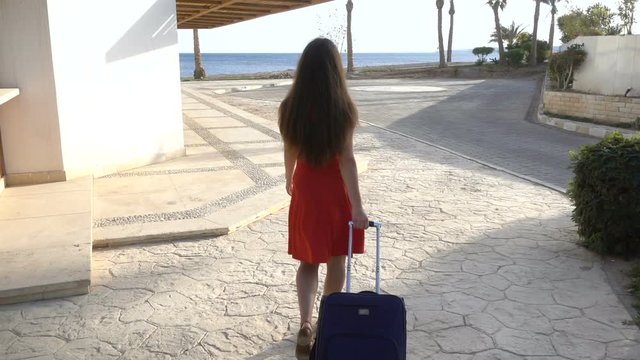 Young girl in red dress traveling on street with suitcase