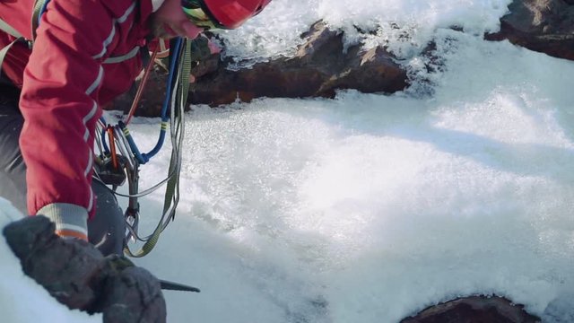 climber down the mountain crevice, leaning on his hand and an ice pick. he has a backpack on his shoulders and safety belts and carabiners on his chest.