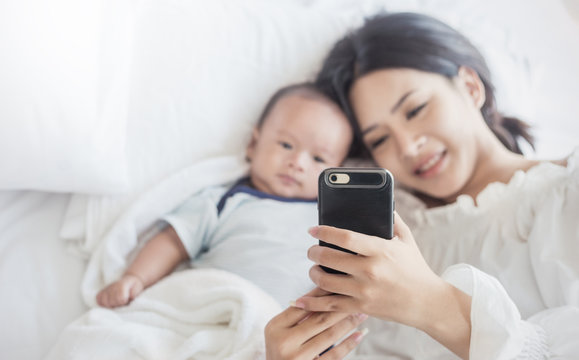 Mother taking picture her newborn baby boy in bed with smart phone. Baby boy taking selfie with cell phone camera. Technology digital communication with people concept