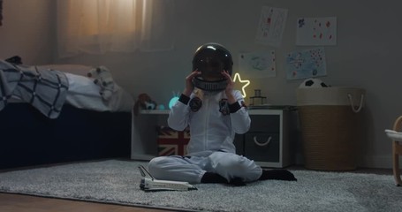 Cute little child girl wearing astronaut suit playing with toy shuttle space ship rocket at home, bedroom interior evening shot. 4K UHD RAW FOOTAGE