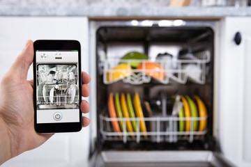 Person Operating Dishwasher With Smartphone