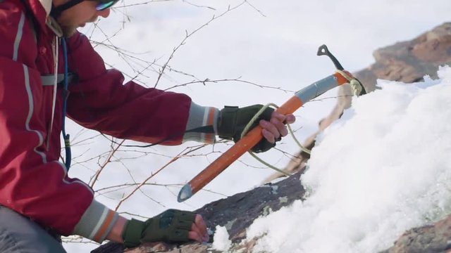 extreme tourist breaks the durable snow with a crevice ice pick. he's wearing a red special suit, backpack and insurance.