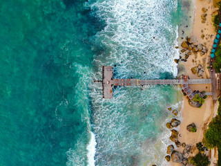 Aerial view of dock over tropical blue water and sand beach, with waves. Wooden pier in the sea. top drone view wooden jetty in blue water in Bali, Indonesia