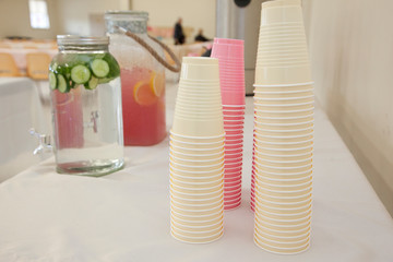 pink and white plastic cups ready to be filled from a container of cucumber water