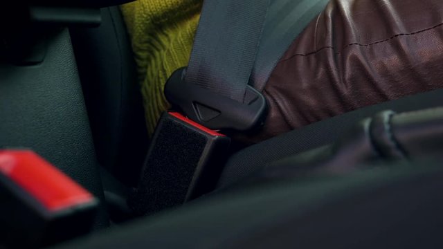 Close up of female hand fastening car safety seat belt while sitting inside of vehicle before driving