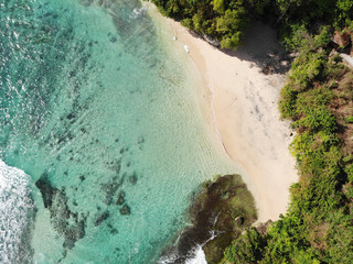 Aerial view of an amazing nature scenery with rock cliff on sandy coastline. Beautiful sea water with waves for surfing in summer season in Bali. Beauty Indian ocean landscape, holiday destination