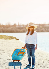 Cute little girl in hat with suitcase on the beach. Summertime concept.