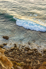ocean wave with foam, water on rocky shoreline from cliff top 