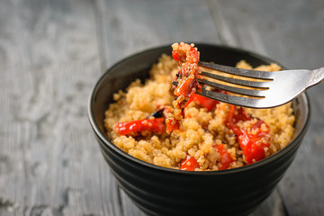 Iron fork in a bowl of boiled quinoa and baked vegetables. Vegetarian dish.