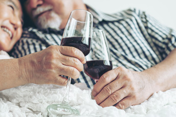 Happy love Elderly couple smile holding a wine glass , Senior couple old man and senior woman relaxing On the bed in the bedroom Celebrate the wedding anniversary - lifestyle senior concept