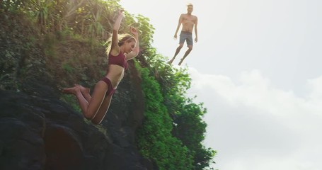 Young attractive couple cliff jumping into ocean with jungle background, man and woman jumping off of cliff together, summer adventure freedom