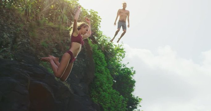 Young attractive couple cliff jumping into ocean with jungle background, man and woman jumping off of cliff together, summer adventure freedom