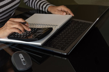 Casual business woman or accountant hand using calculator to calculate about income and writing note on notebook, work on laptop computer at modern home office. e business, e commerce concept.
