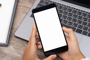 Woman hand holding and using mobile smart phone with blank white screen ,work on laptop computer with cup of coffee on the wooden table. online shopping,digital marketing concept.