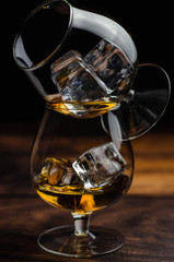 Two whiskey / cognac glasses with ice on a wooden background. Dark backdrop.