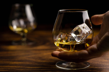Whiskey / cognac glass with ice in a hand on a wooden background. Dark backdrop.