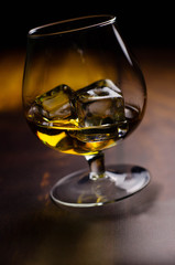 Whiskey / cognac glass with ice on a wooden background. Dark backdrop.