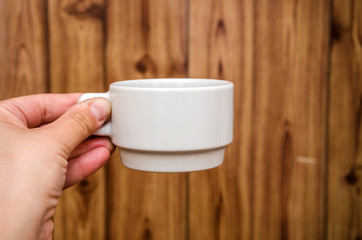 white cup in hand on wooden background