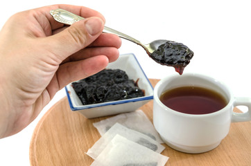hand holding a spoon with jam on the background of a cup of tea