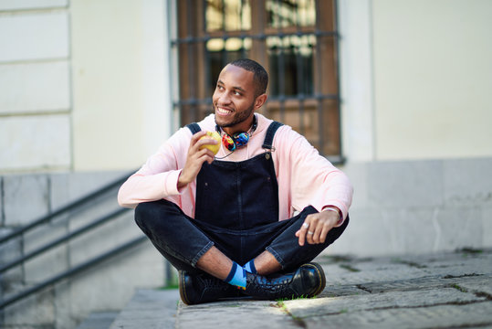 Young black man eating an apple sitting on urban steps. 
