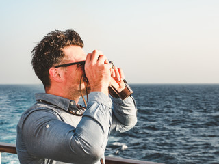 Attractive man holding a vintage camera on the empty deck of a cruise liner against a background of sea waves. Side view, close-up. Concept of leisure and travel