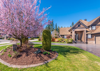 Beautiful exterior of newly built luxury home. Yard with green grass and walkway lead to ornately designed covered porch and front entrance.