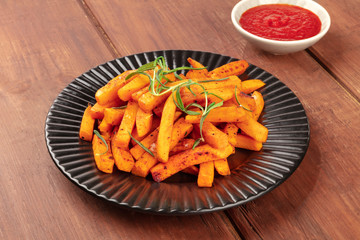 Sweet potato fries with rosemary and ketchup on a dark rustic wooden background