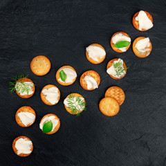 Salt crackers with soft cream cheese spread and herbs, shot from the top on a black background with copy space