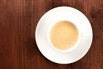 A cup of coffee with froth shot from the top on a dark rustic wooden background with a place for text