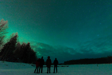 Four people has looking the northern lights Aurora Borealis at Kuukiuru village lake in Lapland, Finland.
