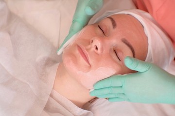 Facial massage for a woman in a beauty salon. Beautician rubs moisturizer in the face of the girl...