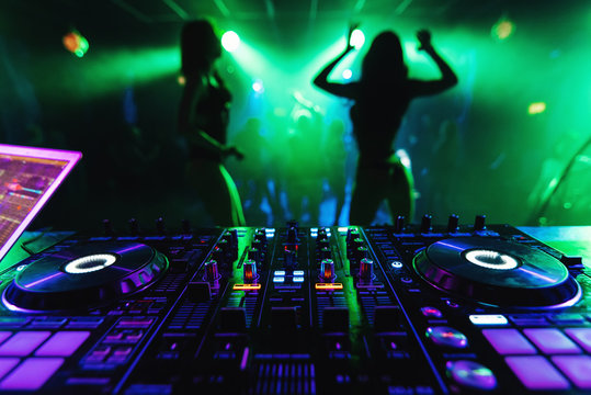 DJ mixer in a nightclub with dancing on the background of go-go dance girls