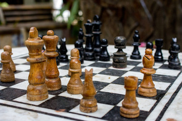 Outdoor chessboard with black and yellow figures with unfocused background. Competition and strategy concept. Intelligent sport. Defeat and fight concept. Chess wooden pieces on board. 