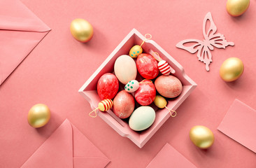Easter flat lay on coral color paper with wooden tray full of decorative eggs, greeting cards, with envelopes and decorative flowes