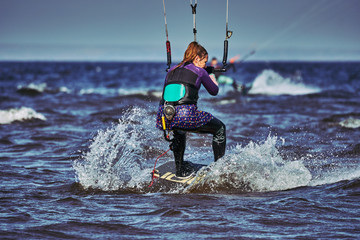 A female kiter slides on the surface of the water. Splashes of water fly apart. Close-up.