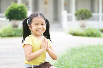 Asian child smiling hand in hand or kid girl pay obeisance and pray or hello welcome and thank you with wear yellow shirt in morning at hotel and church or temple for peace on lawn and receptionist