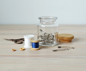 Glass jar, metal pins, thread, scissors and buttons on the wooden table