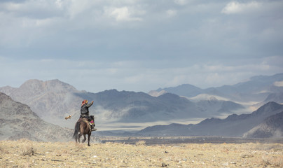 kazakh eagle hunter traveling on hgis hotse in a landscape of altai Mountains