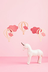 Cute white unicorn over the pink pastel background with clouds and ballons