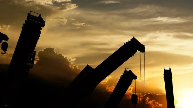 Idle construction cranes over sunset.
