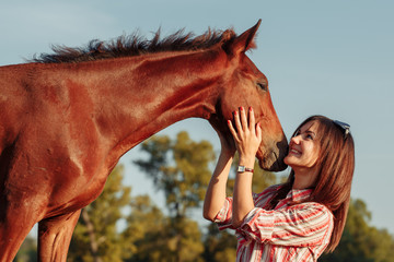 Young pretty woman hugs a foal in a field. Summer time.