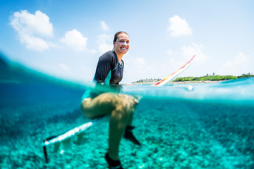 Happy lady surfer sits on the surfboard, smiles and looks at the camera . Splitted image with underwater view